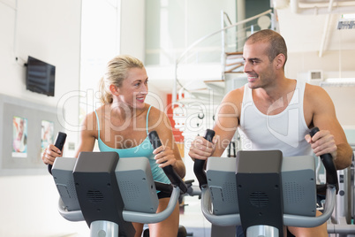 Fit couple working on exercise bikes at gym