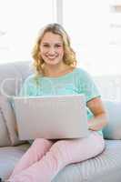 Smiling casual blonde sitting on couch using laptop