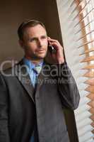 Businessman peeking through blinds while on call