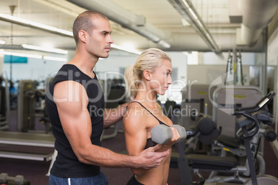 Male trainer assisting woman with dumbbell in gym