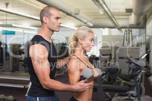 Male trainer assisting woman with dumbbell in gym