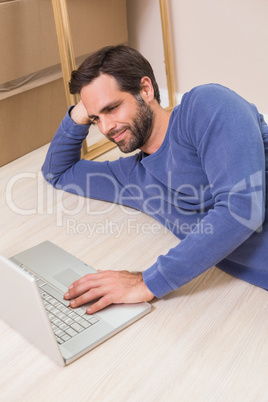 Happy man lying on floor using laptop