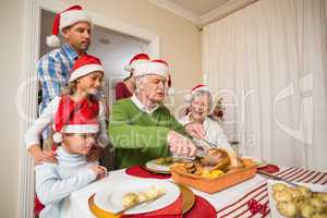 Grandfather in santa hat carving chicken at christmas