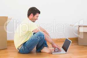 Casual man sitting on floor using laptop at home