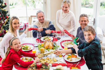 Family pulling christmas crackers at the dinner table