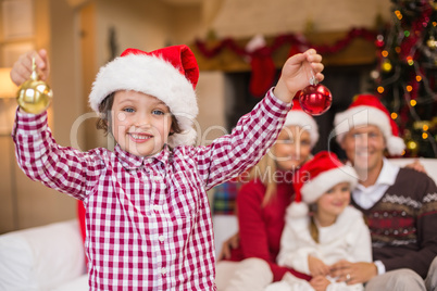 Son wearing santa hat holding baubles in front of his family