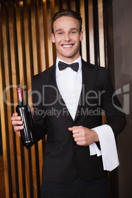 Handsome waiter holding a bottle of red wine and a towel