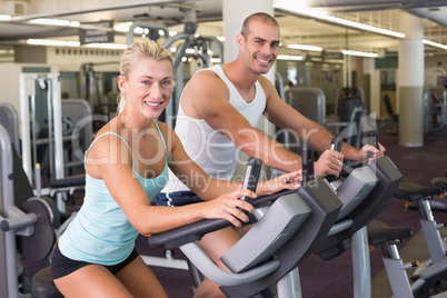 Fit young couple working on exercise bikes at gym