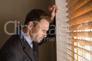 Serious businessman peeking through blinds