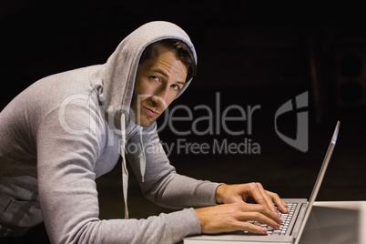 Man in hood jacket hacking a laptop while looking at camera