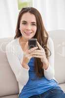 Pretty brunette sending a text on the couch