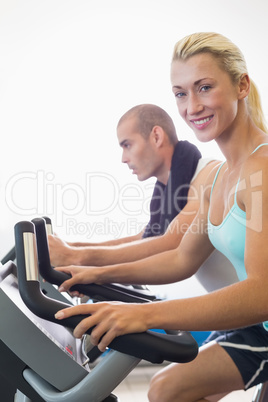 Fit couple working on exercise bikes at gym