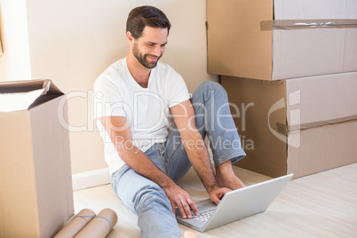 Happy man using laptop surrounded by boxes