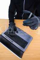 Mid section of a burglar using laptop and smartphone