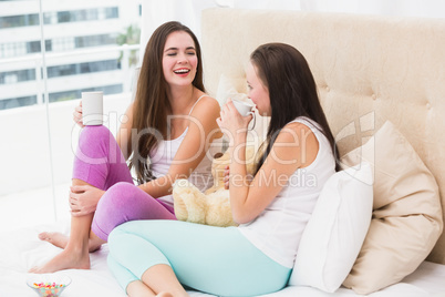 Pretty friends having coffee on bed