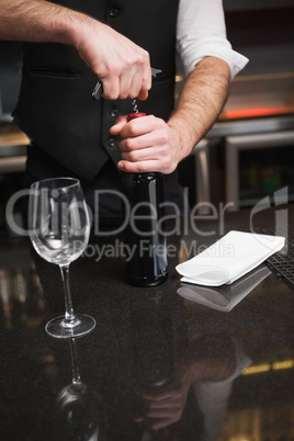 Handsome waiter opening a bottle of red wine