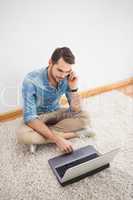 Casual man sitting on floor using laptop on the phone