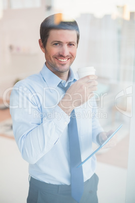 Smiling businessman holding tablet and disposable cup looking ou