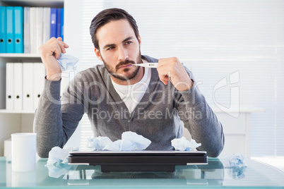 Thoughtful businessman holding pen at desk
