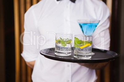 Cheerful young waiter holding tray with cocktails