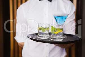 Cheerful young waiter holding tray with cocktails