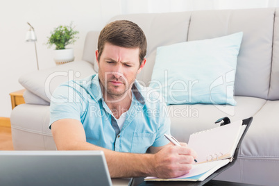 Focus man looking at is laptop and writing on a notebook