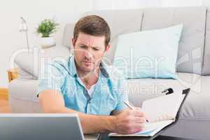 Focus man looking at is laptop and writing on a notebook