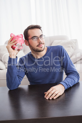 Young man shaking his piggy bank