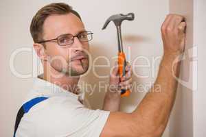 Handyman hammering nail in wall while looking at camera