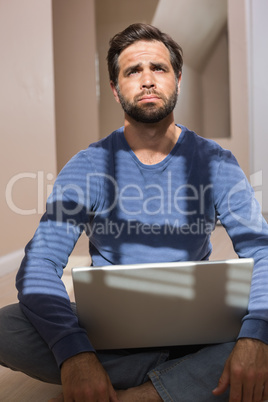 Depressed man sitting on floor using laptop