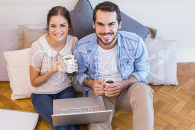 Cute couple sitting on floor using laptop