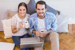 Cute couple sitting on floor using laptop