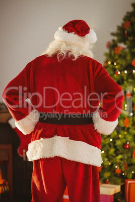 Rear view of santa standing in front of the christmas tree