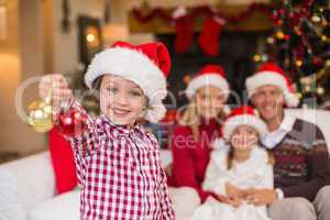 Son wearing santa hat holding baubles in front of his family