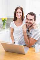 Young couple smiling at the camera using laptop