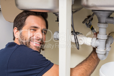 Happy plumber fixing under the sink