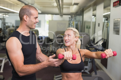 Male trainer assisting woman with dumbbell in gym