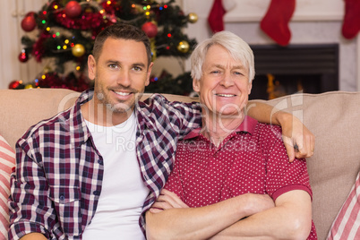 Father with arm around grandfather posing on sofa