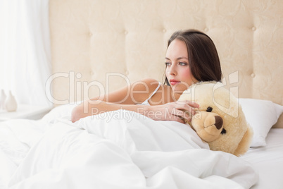 Pretty brunette under the duvet with teddy bear