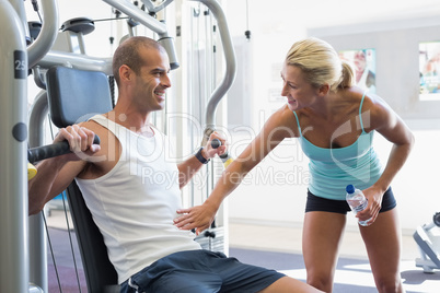 Trainer assisting man on fitness machine at gym