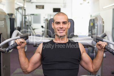 Smiling young man working on fitness machine at gym