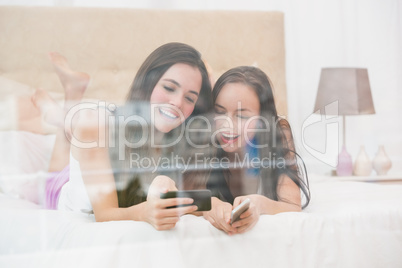 Pretty friends looking at smartphone on bed