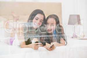Pretty friends looking at smartphone on bed