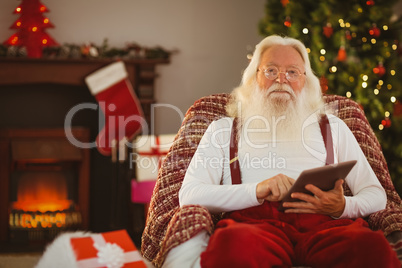 Smiling santa using tablet on the armchair