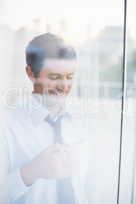 Smiling businessman holding mug seen through window