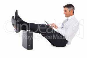 Businessman sitting with foot on briefcase and using tablet
