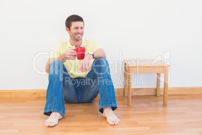 Casual man sitting on floor holding a mug at home Casual man sitting on floor holding a mug at home
