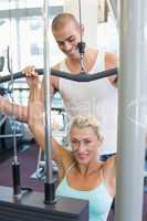 Male trainer assisting woman on lat machine in gym
