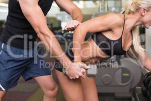 Male trainer assisting woman with dumbbell in gym