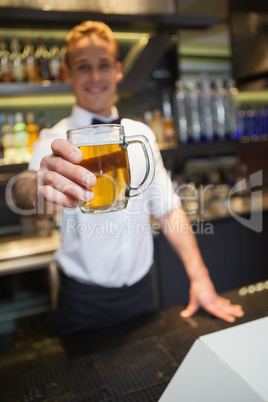 Smiling bartender offering pint of beer to camera